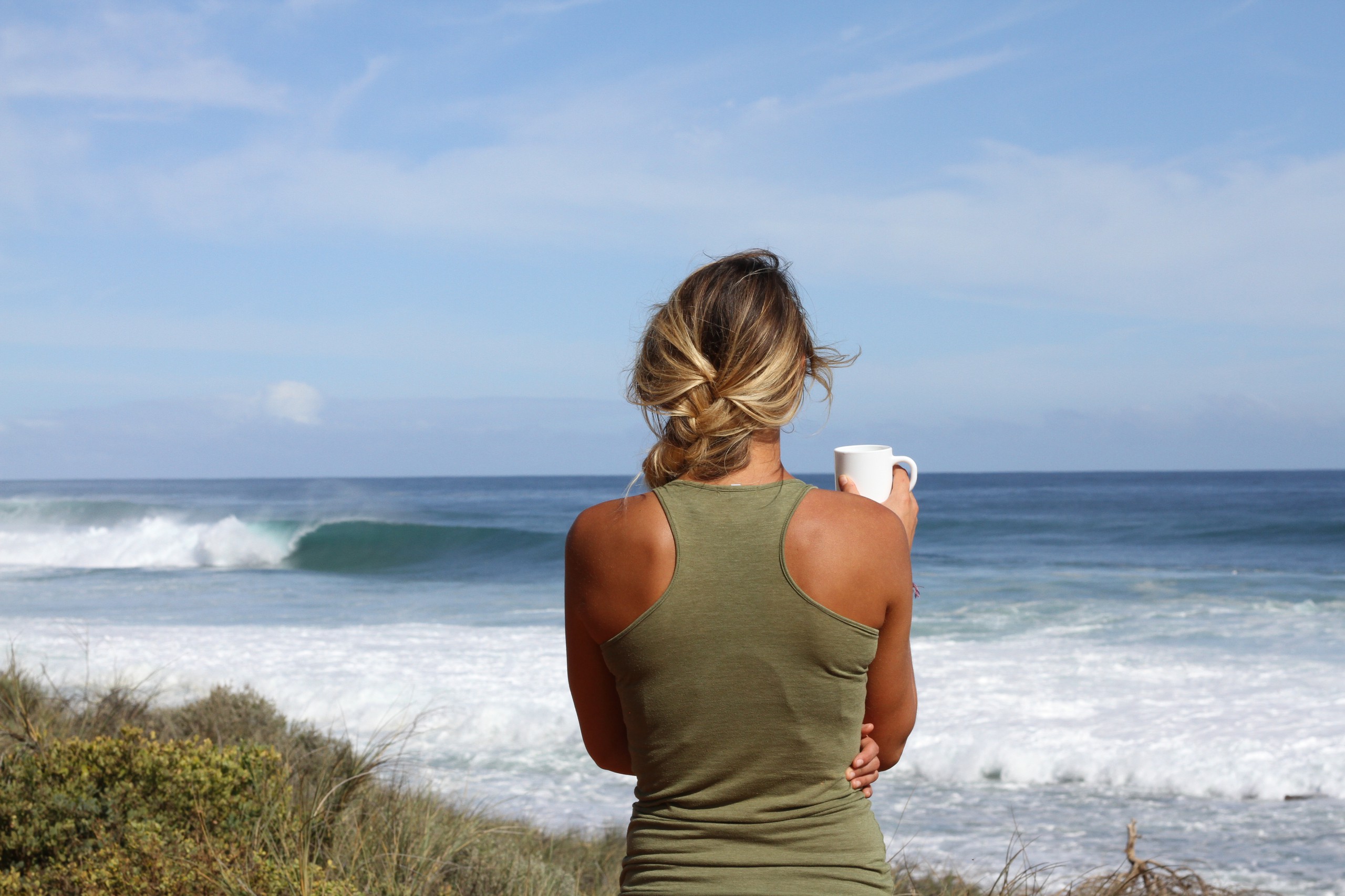 Woman holding a mug by the ocean practicing mindful breathing